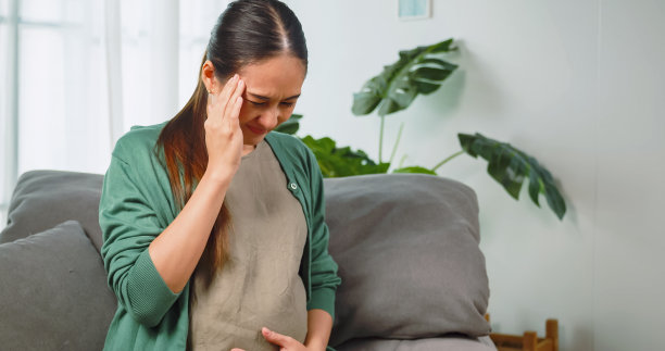 亚洲孕妇躺在家里的沙发上休息时感到恶心和头痛。图片下载