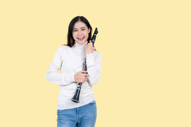 一个迷人的亚洲女音乐家站在一个孤立的黄色背景下与单簧管。图片下载