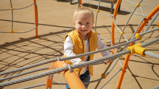可爱活泼的小男孩在操场上爬绳梯的照片。孩子们在户外玩耍，孩子们在户外，暑假和假期。图片下载
