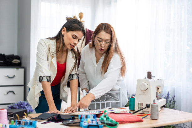 不同的女性时装设计师在裁缝工作室设计服装。迷人的年轻女裁缝师团队感到快乐，享受在车间商店设计新款式的衣服。图片下载