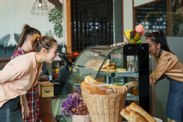 两个漂亮的亚洲女顾客，走进咖啡馆直奔面包店的蛋糕柜，里面有很多糖果，漂亮的店主拿着蛋糕托盘，微笑着迎接顾客点单。图片下载