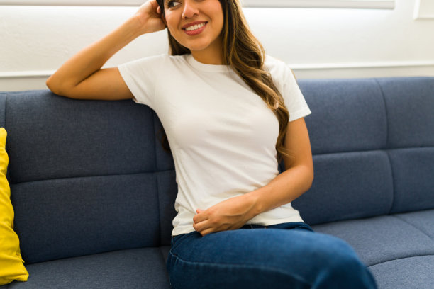 一个微笑的女人坐在沙发上，穿着一件白色的模拟t恤图片下载