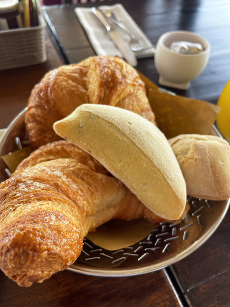 餐巾纸衬里的特写图片，圆形不锈钢篮子里装着一堆新鲜出炉的意大利面包卷和羊角面包，开胃面包，餐厅桌子背景，高架视图图片下载