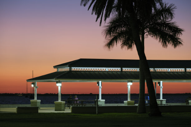 日落时分，人们在公园海边凹形屋顶下休息的黑暗剪影图片下载