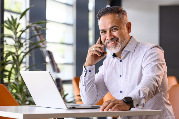 一个面带微笑的成熟商人的肖像，手提电脑在听他的手机图片下载