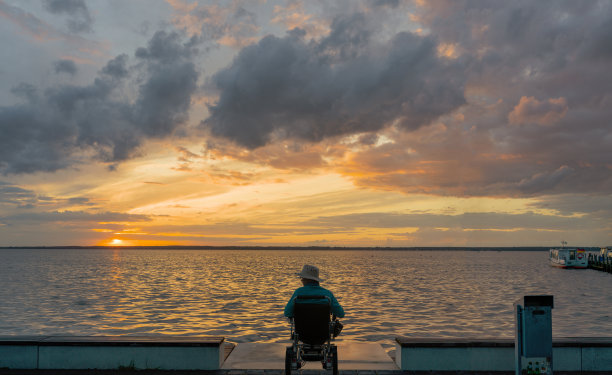 黄昏时分，一位老人坐在轮椅上，欣赏着雄伟的云景图片下载
