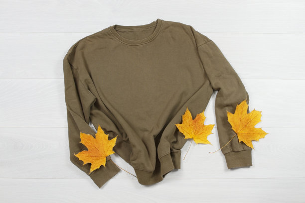 靠近卡其布空白模板运动衫帽衫复印空间。秋天的黄叶。顶视图模型运动衫套头衫，白色木制背景。休闲衬衫套装。平铺模板落衣图片下载