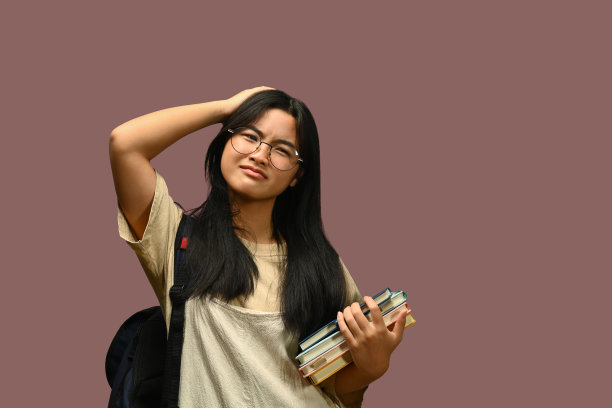 困惑的少女背着双肩包和粉红色背景的书。学习、育人、回校的理念图片下载