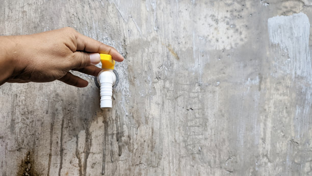 一个男人的手握着水龙头，背景是长满青苔的、没有粉刷的墙壁。图片下载