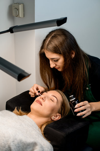 专业女美容师用棉签轻轻擦拭客户面部图片下载