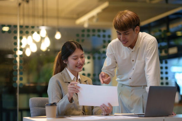 两位年轻的亚洲商人讨论投资项目工作和规划策略。商人和女商人在办公室用笔记本电脑聊天。图片下载