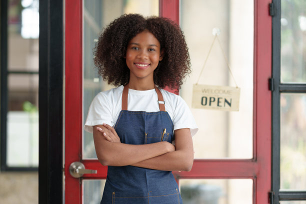 微笑的女店主站在那里等着开店，等着接受客户服务，并打开商店的招牌。图片下载