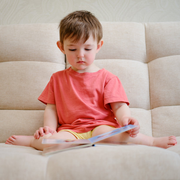 可爱的宝宝在玩那本五颜六色的绘本，翻着书页，摸着图画。这个小孩坐在家里看书时陷入了沉思。图片下载