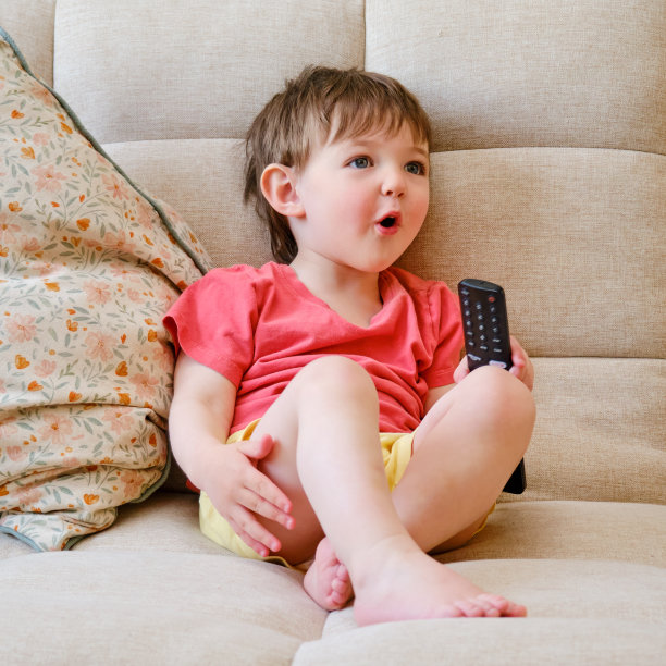 看电视上的卡通片给宝宝带来了很多快乐，因为他们坐在沙发上，手里拿着遥控器。两岁左右(一岁十个月)图片下载