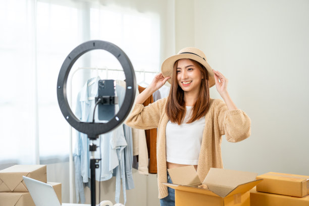 年轻的亚洲女企业主在时尚商店使用手机直播销售时尚帽子和服装。有影响力的人录制视频评论物品在社交媒体上出售。网上购物图片下载