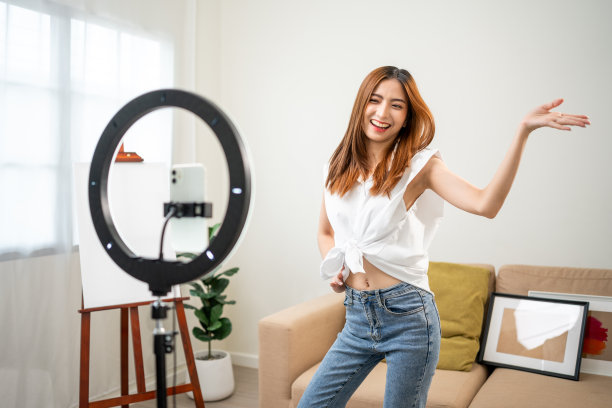 年轻的时尚影响者亚洲女人在家里的客厅里用手机跳舞。创作者，视频博主，才艺舞蹈，享受爱好，内容录制，展示视频分享在社交媒体上。图片下载