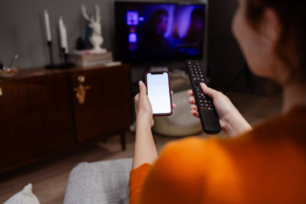 一个年轻的白人女人拿着手机换着电视频道图片下载