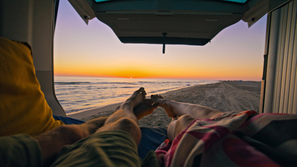 一对夫妇躺在露营车里享受日落时分的海滩图片下载