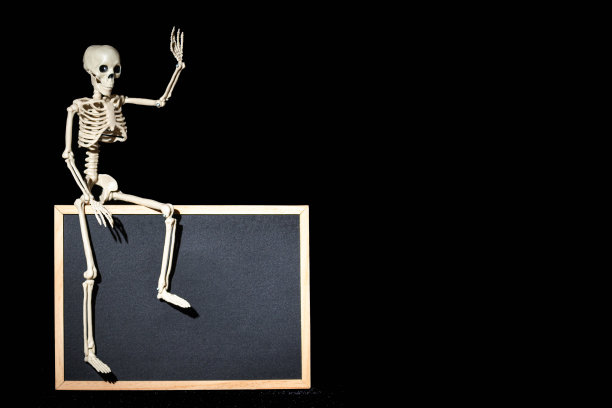 搞笑的人体骨架坐在黑色背景的空白黑色挂图上，复制空间，模型图片下载