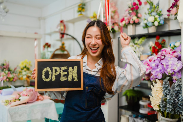 微笑的亚洲年轻女子在花店工作时向客户卖花。客户通过手机银行支付。图片下载