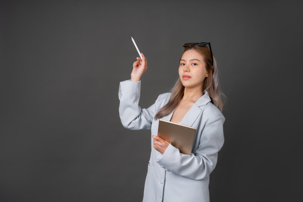 留长发的亚洲女性高管或公司员工戴时尚眼镜，穿蓝色西装。在你身边放一个平板电脑，在灰色背景的工作室里拍一张照片图片下载