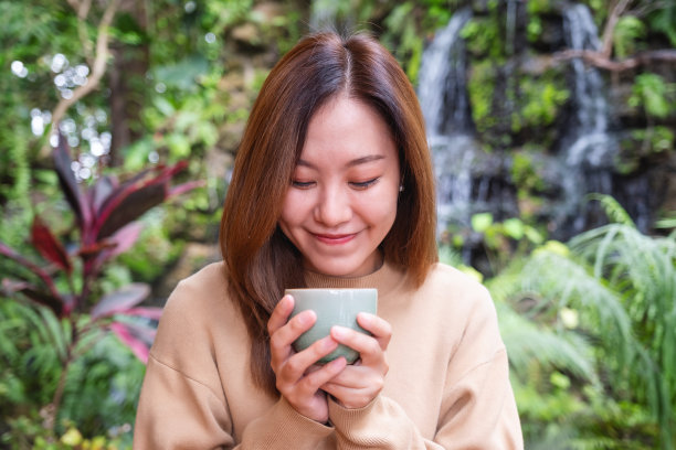 年轻女人在花园瀑布旁喝咖啡的肖像照图片下载
