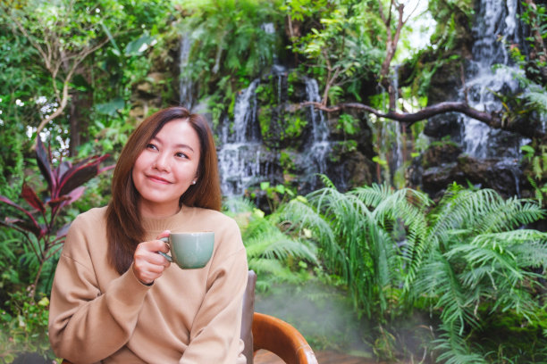 年轻女人在花园瀑布旁喝咖啡的肖像照图片下载