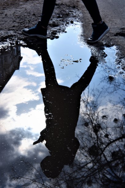 在一个下雨天，一个小女孩手里拿着手机，在水里跳过水坑图片下载