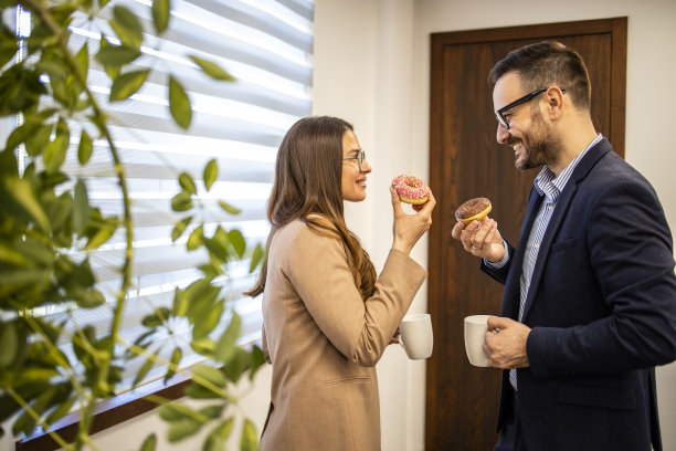 两个商人在公司办公室里聊天，吃着甜甜圈。图片下载