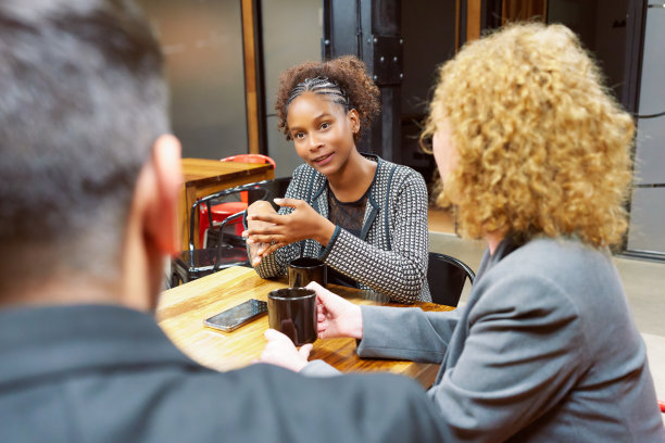 年轻的黑人妇女坐在会议上与一群商界人士交谈图片下载