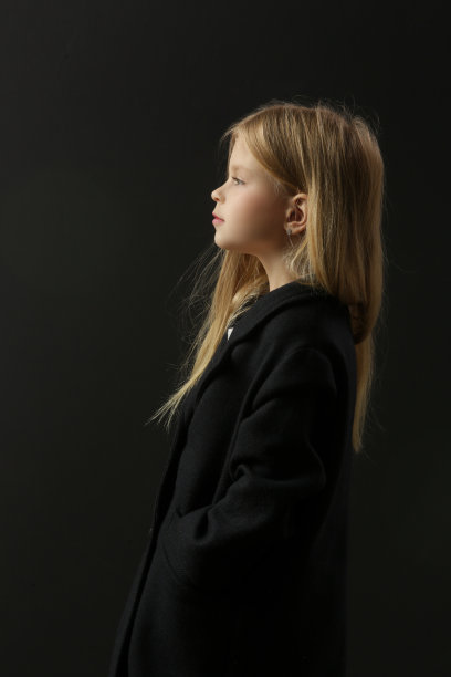 侧视图肖像可爱的小女孩在黑色的工作室背景黑色外套图片下载