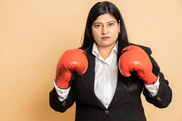 愤怒的年轻印度员工戴着拳击手套，在米色背景中孤立地打拳，沮丧的女商人。工作负载,图片下载
