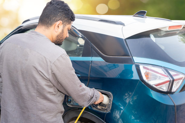 一名印度男子将电源线插入插座，在户外充电站为他的现代电动汽车充电。电动汽车充电电池充电口。可再生能源或绿色能源。图片下载