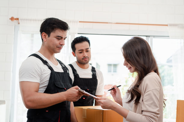 一名妇女一边检查，一边把箱子和家具从一辆小货车上卸到一所有服务货物的新房子里，两名穿着制服的搬运工正在搬运箱子。搬家和送货的概念。图片下载
