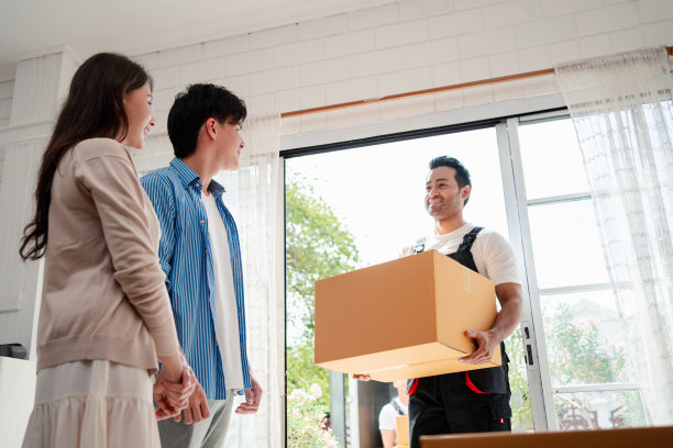 一对亚洲夫妇一边检查，一边把箱子和家具从一辆小货车上卸到一所有服务货物的新房子里，两名穿着制服的搬运工搬运箱子。搬家和送货的概念。图片下载