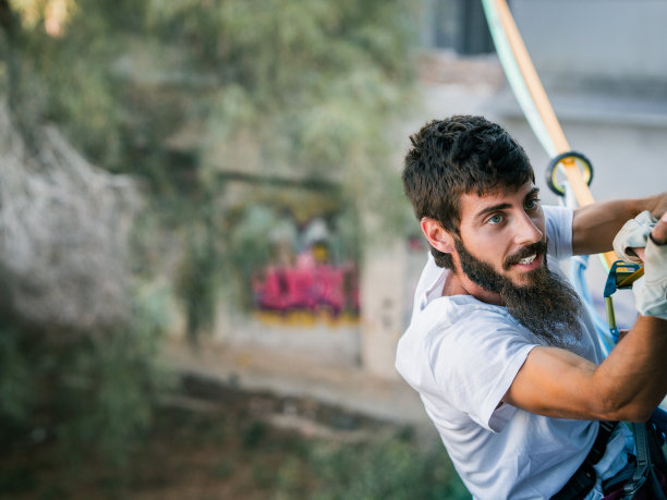 一个白人男孩带着手套和救生绳等保护系统攀岩图片下载