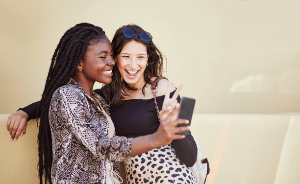 最好的朋友在户外自拍时玩得很开心，并展示了和平的手势。两个多民族女性朋友在城市里共度时光，用智能手机为社交媒体拍照图片下载