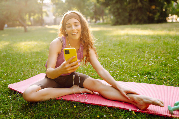 年轻的健身女性戴着耳机，在早晨的瑜伽练习中使用智能手机。图片下载