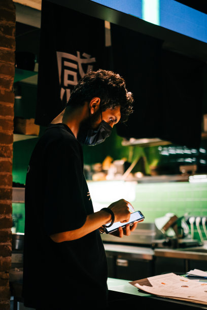 年轻的白人亚洲人在小酒馆工作，用手机在大厅里接受网上的外卖订单或确认客人的订单。图片下载