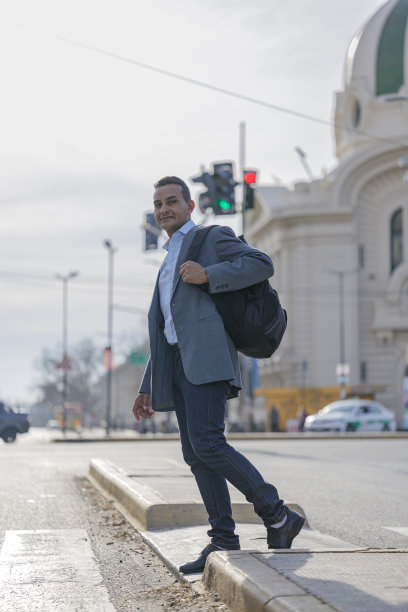 穿着西装背着背包的拉丁裔男子穿过城市的人行道。图片下载