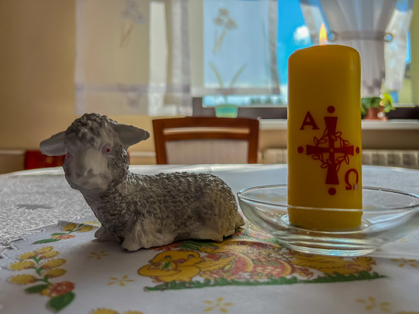 一只谦虚的小羊羔和一支点燃的蜡烛站在桌子上作为复活节的象征。图片下载