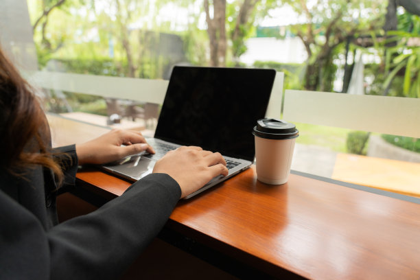 一杯咖啡在她身边，一个年轻女子的手优雅地操纵着笔记本电脑，沉浸在网上购物的便利和兴奋中，她探索着一个充满无限可能性的世界。图片下载