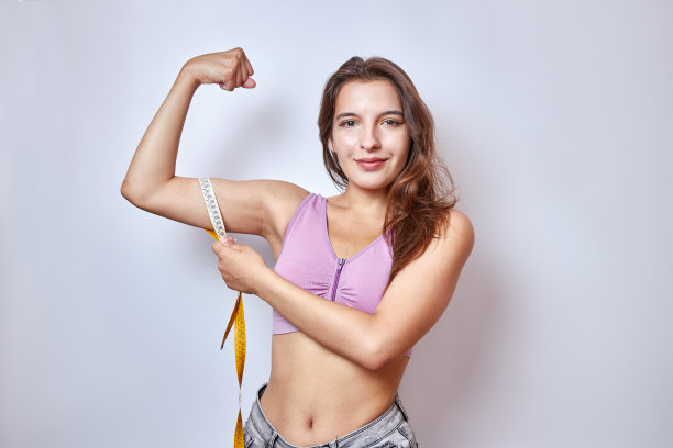 一个漂亮的女孩用卷尺测量身体肌肉的比例。图片下载