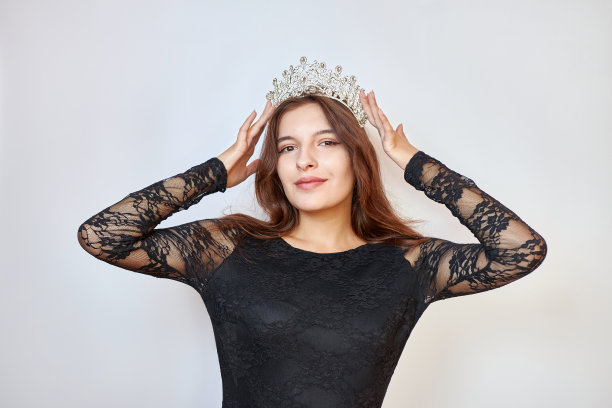 一个穿着黑色连衣裙的漂亮女孩用手捧着一顶皇冠。选美比赛的概念。胜利者的情绪。图片下载