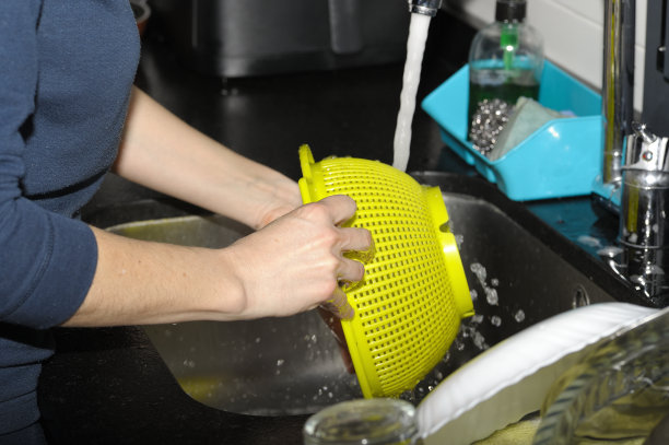 照片上，一个无法辨认的年轻女子正在厨房水槽水龙头上擦拭黄色滤嘴。认不出来的女人。特写照片。有选择性的重点。要复制的空间。图片下载
