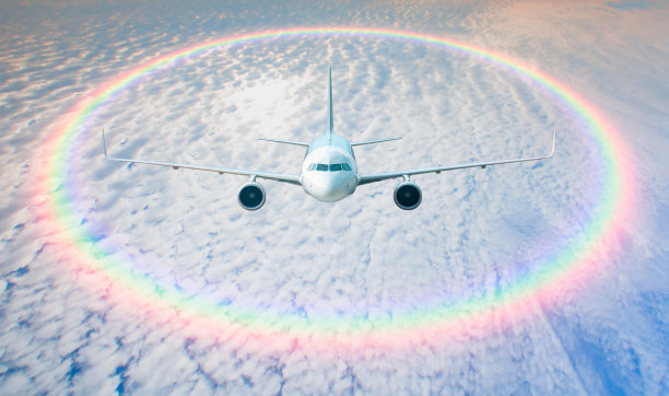 白色的客机在云层下形成了令人惊叹的圆形彩虹——乘飞机旅行图片下载