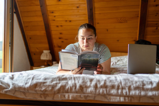 穿着随便的年轻女子躺在小木屋的床上看书图片下载