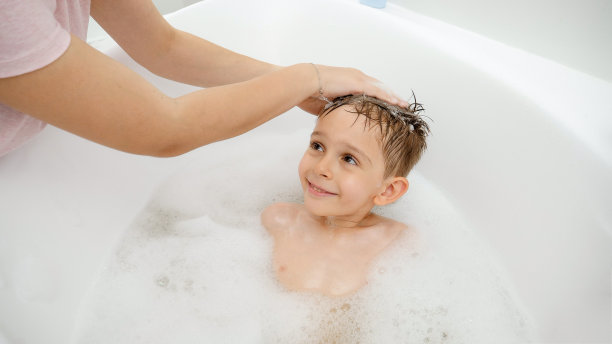 可爱的男孩微笑着在浴缸里洗头，看着他的妈妈图片下载
