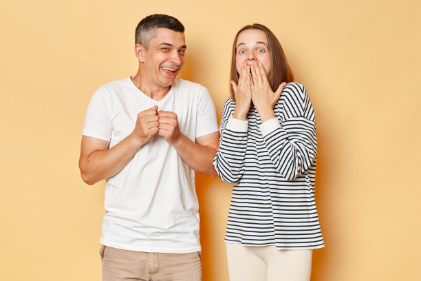 滑稽的夫妇笑着的男人和惊讶的女人穿着休闲服孤立地站在米色背景上，摆出不同的情绪。图片下载