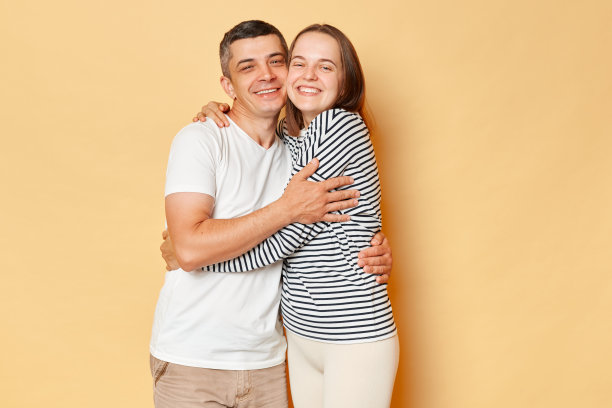 快乐的男人和女人穿着休闲的衣服，孤立地站在米色的背景上，相互拥抱，表达爱意，温柔而浪漫的感觉。图片下载